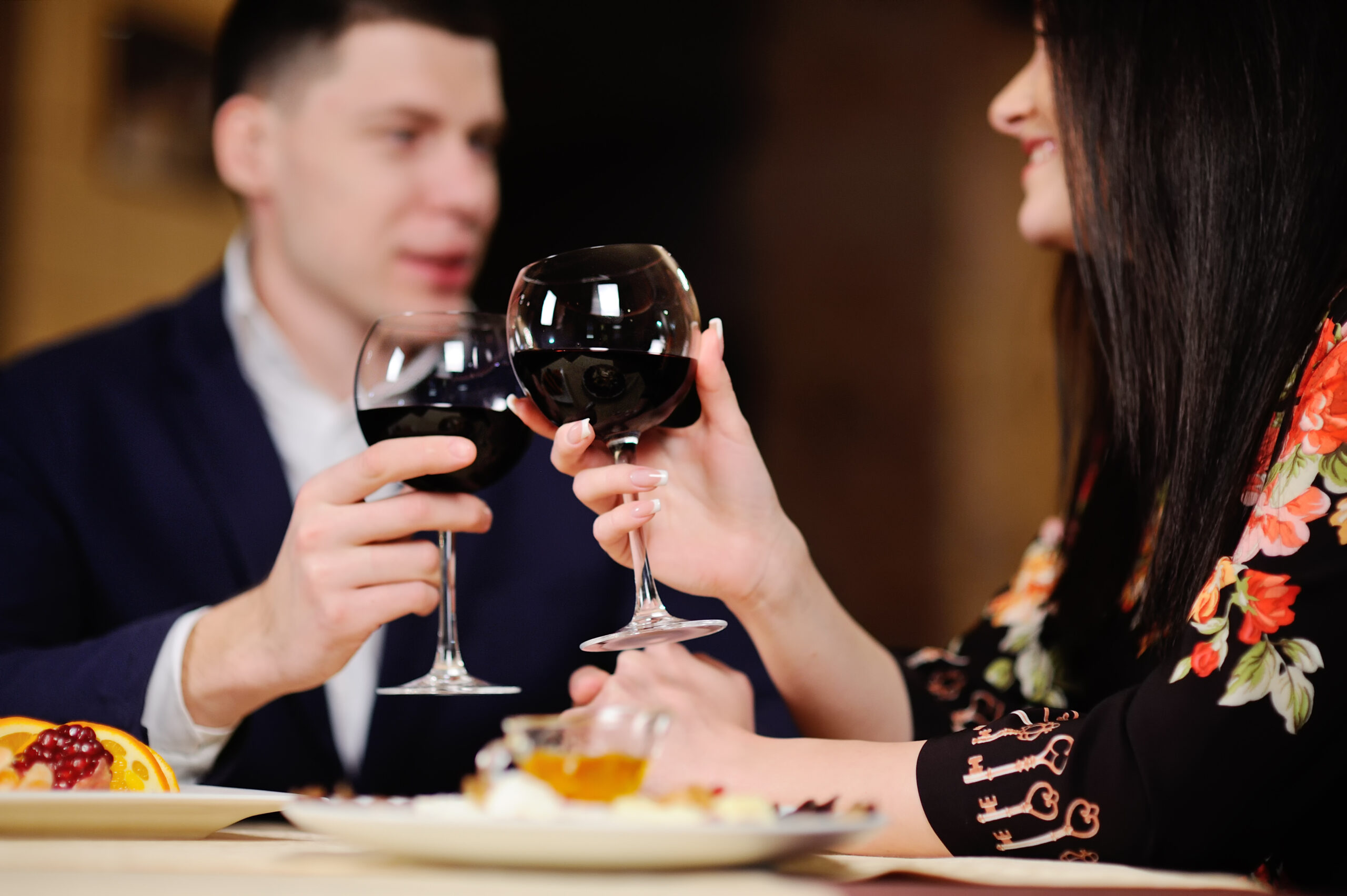 Mann und Frau stoßen in stilvollem Ambiente mit Rotweingläsern an – romantisches Escort-Date in Köln