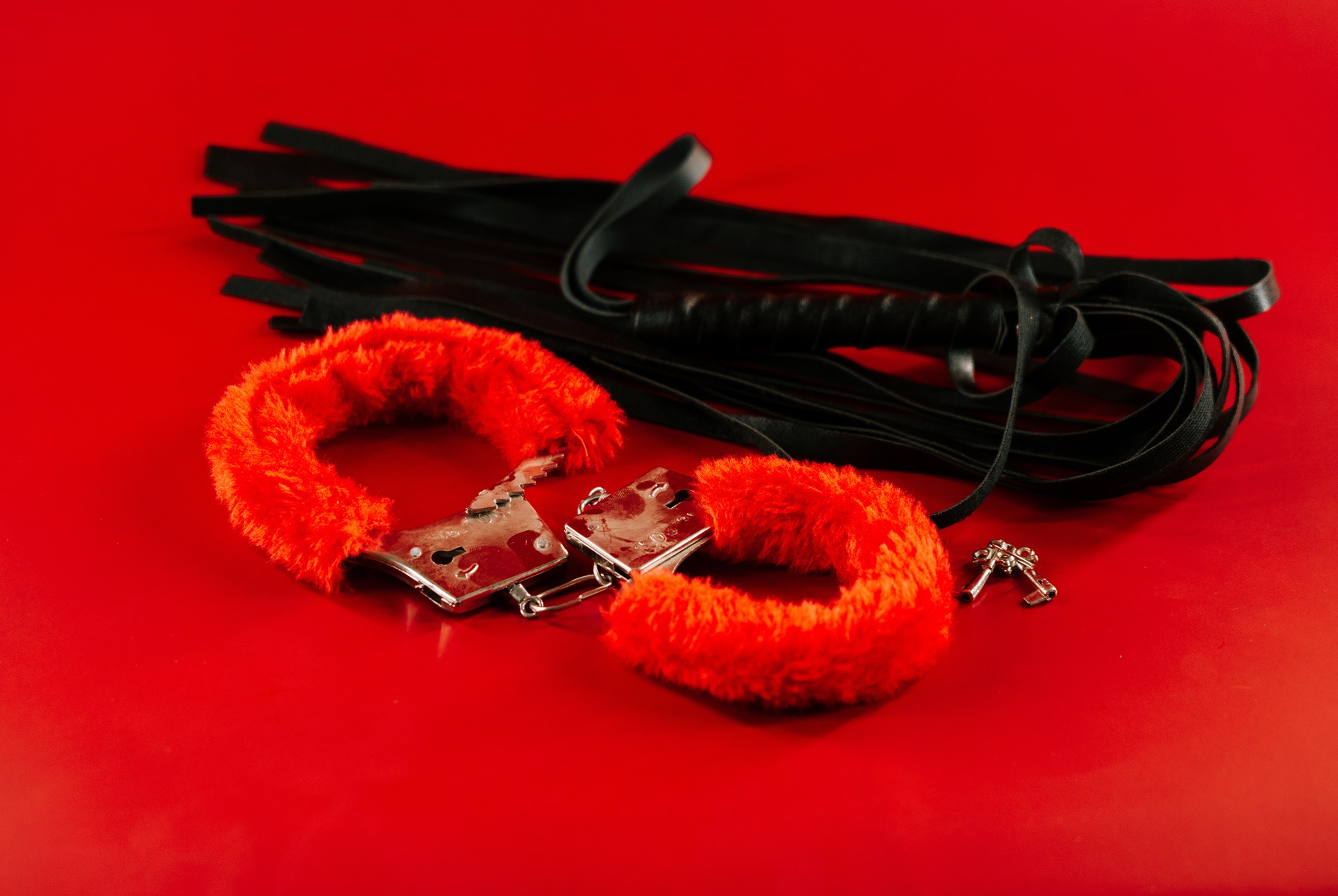 Rote Plueschhandschellen und schwarze Peitsche für sinnliche Spiele | High Class Escort